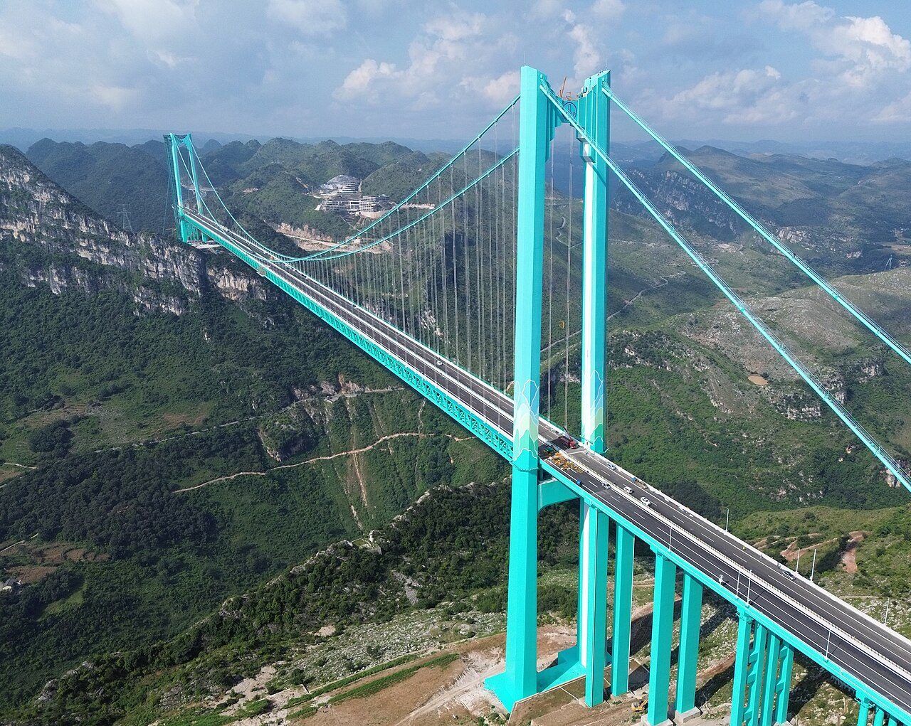 花江大峡谷大桥的航拍图，青绿色桥塔横跨一条深绿色峡谷